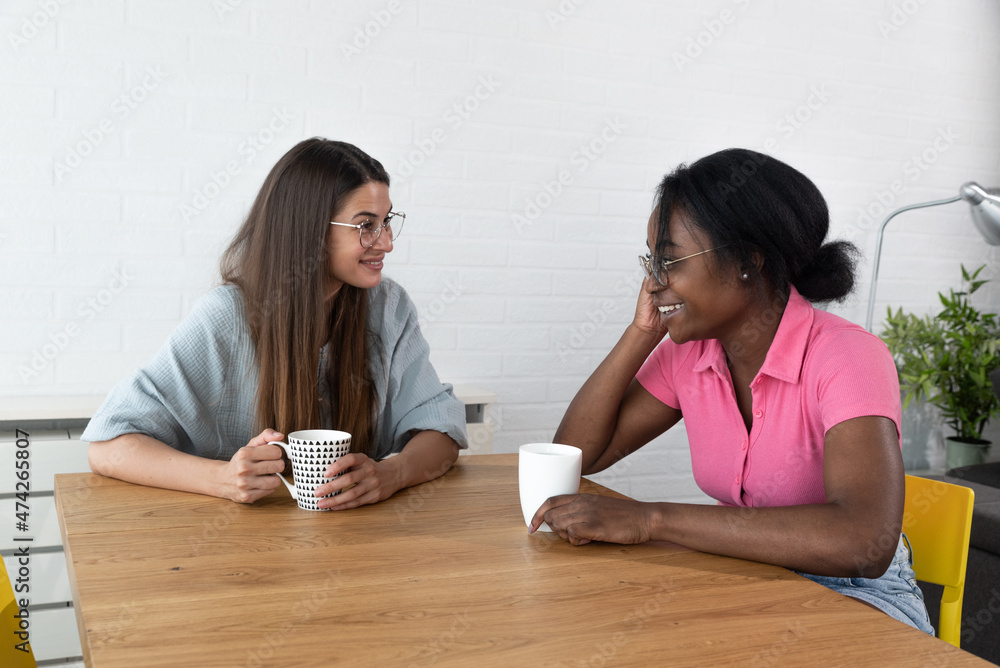 Two best friends hanging out at home together and having fun while sitting in cozy modern apartment, drinking coffee. Two women gossip about the men they met last night out at the party in the club. Two best friends hanging out at home together and having fun while sitting in cozy modern apartment, drinking coffee. Two women gossip about the men they met last night out at the party in the club.