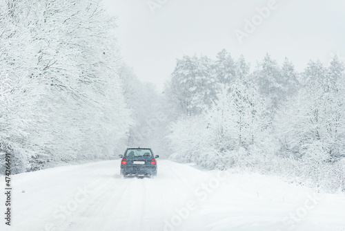 Car driving after heavy snowfall, transportation in winter, road covered in snow, weather problems, driving through winter forest
