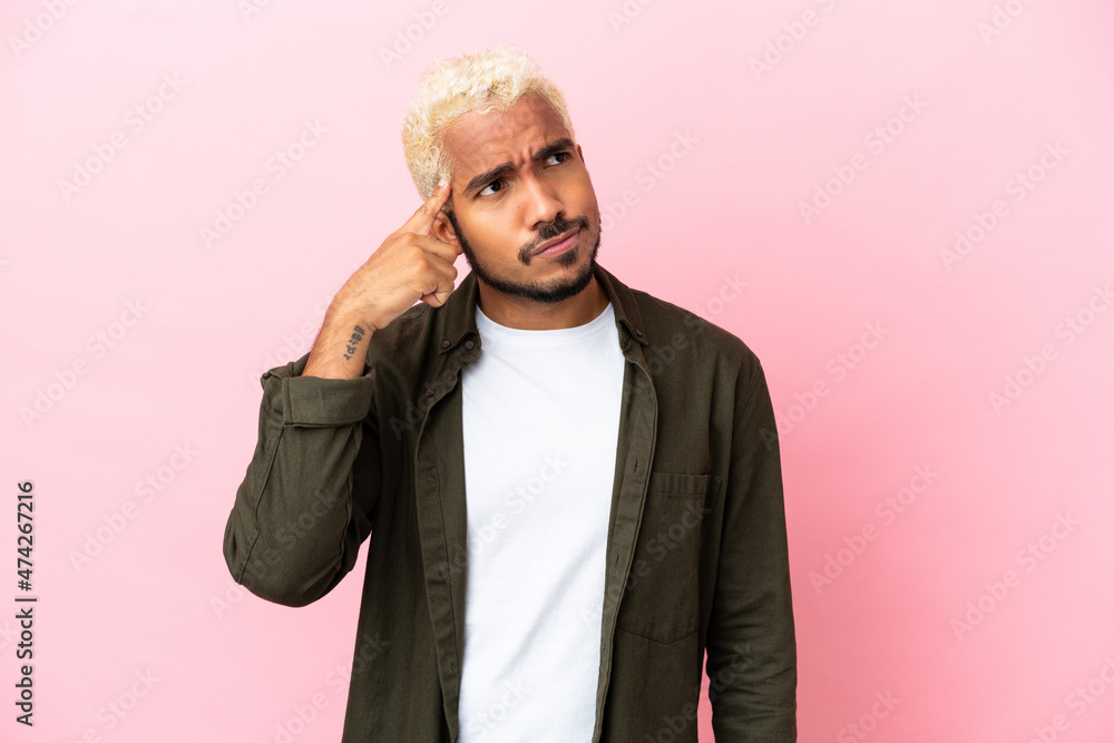 Young Colombian handsome man isolated on pink background making the gesture of madness putting finger on the head