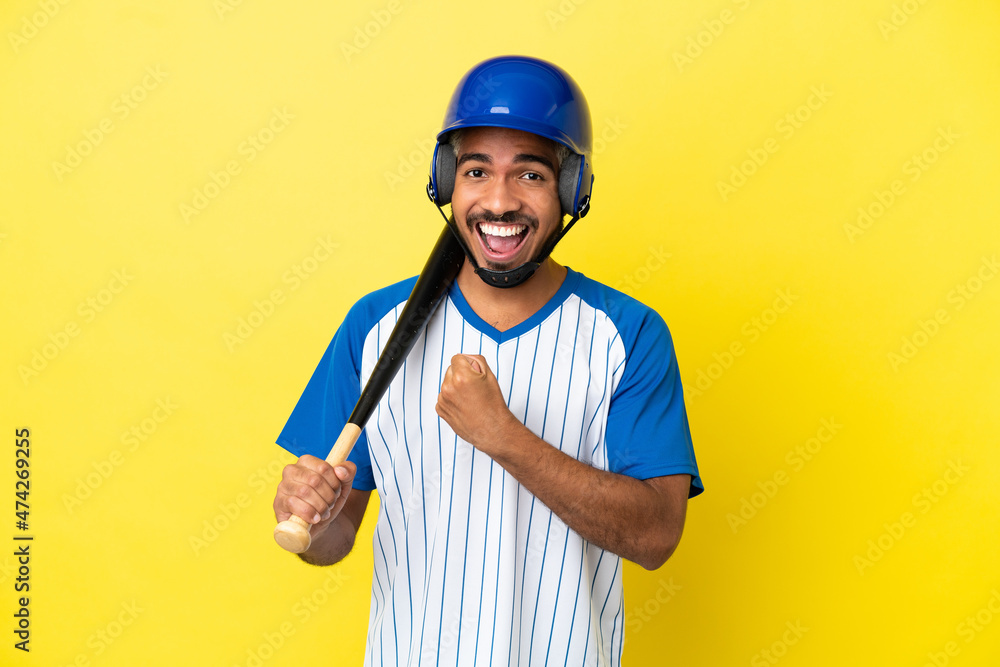 Young Colombian latin man playing baseball isolated on yellow background celebrating a victory