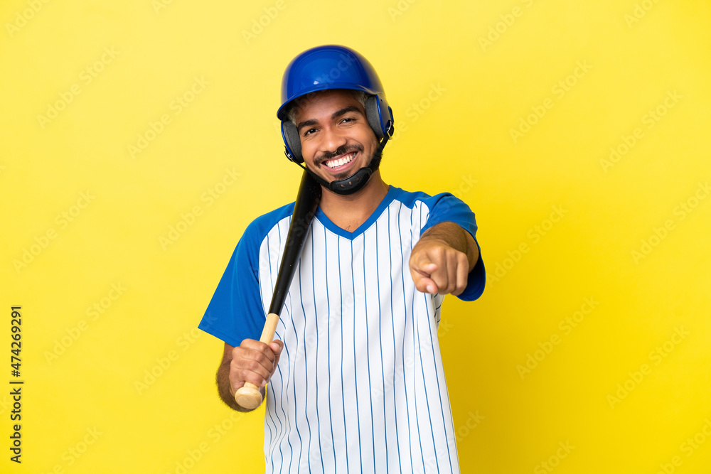 Young Colombian latin man playing baseball isolated on yellow background pointing front with happy expression