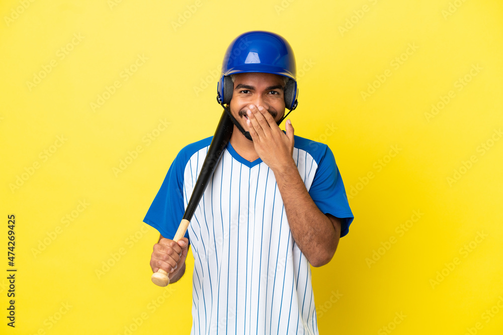 Young Colombian latin man playing baseball isolated on yellow background happy and smiling covering mouth with hand
