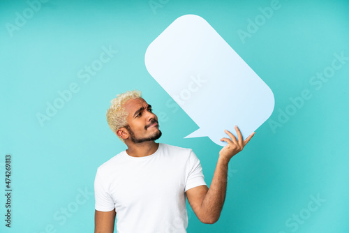 Young Colombian handsome man isolated on blue background holding an empty speech bubble