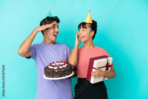 Cuadro en lienzo Young mixed race couple holding birthday cake and present isolated on blue backg