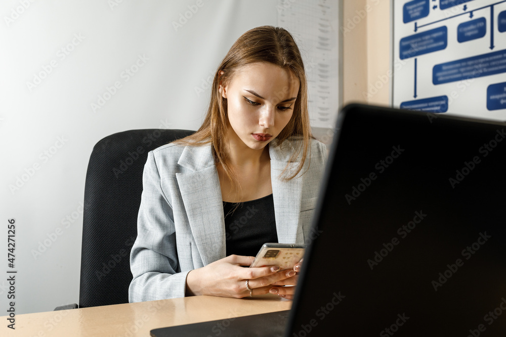 a young female secretary in the office looks at the phone while sitting at the computer a young female secretary in the office looks at the phone while sitting at the computer
