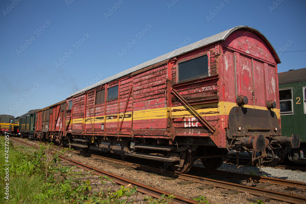 Weathered old wooden train carriage with yellow stripe on the side parked on railway tracks