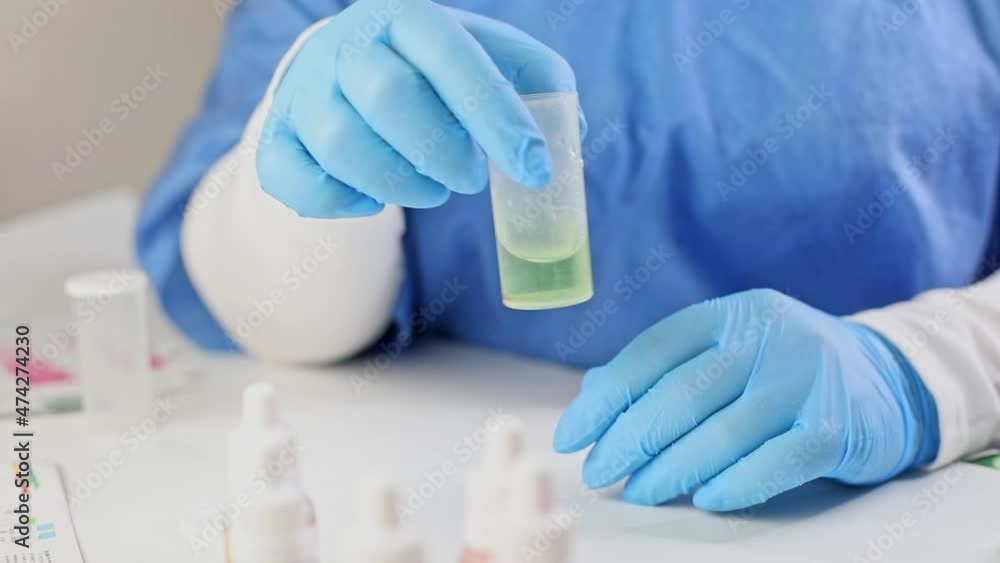 a laboratory assistant in a blue medical suit and gloves conducts water testing, mixes the green reagent with aquarium water in a container for chemical experiments, control the quality of the liquid a laboratory assistant in a blue medical suit and gloves conducts water testing, mixes the green reagent with aquarium water in a container for chemical experiments, control the quality of the liquid