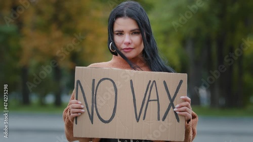 Young confident hispanic woman holding cardboard sign no vax protesting against vaccination outdoors serious girl standing on street demonstrates protest immunization covid19 stop untried vaccine