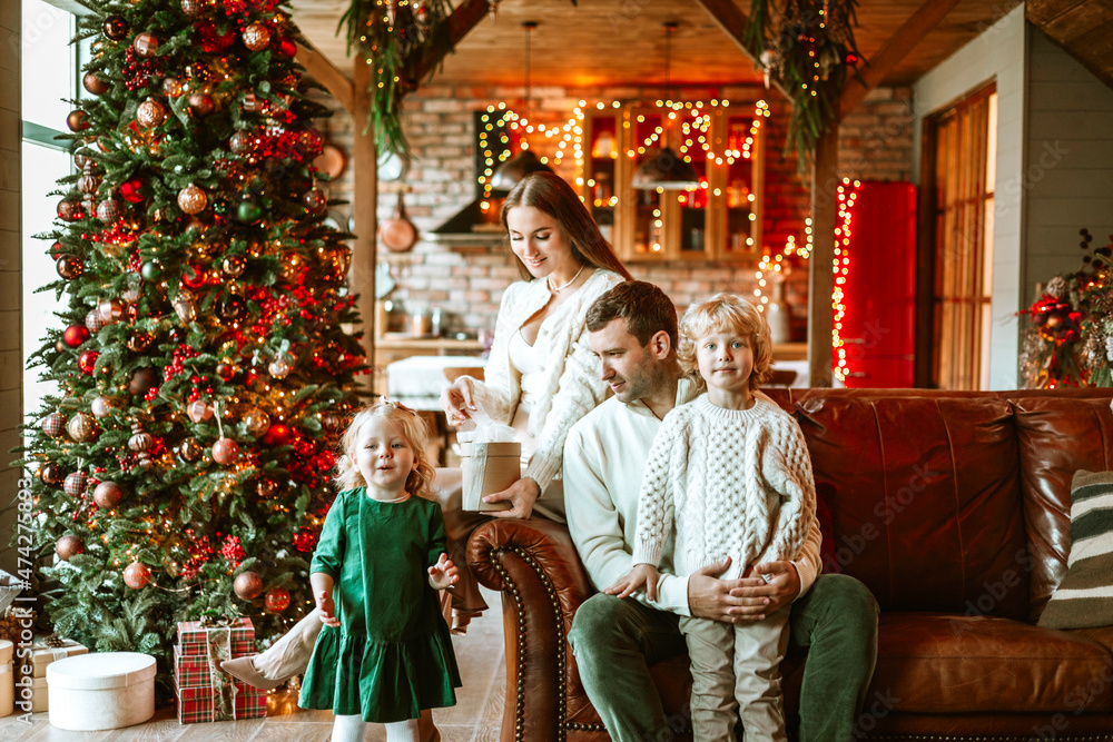 family of four parents pregnant mom and dad and two siblings little boy and girl in stylish clothes in chalet are ready to welcome Christmas and New Year near Christmas tree with gift box presents family of four parents pregnant mom and dad and two siblings little boy and girl in stylish clothes in chalet are ready to welcome Christmas and New Year near Christmas tree with gift box presents
