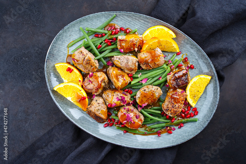 Modern style jusy seared pork pigllet tenderloin fillet meat medallions with orange relish sauce, pomegranate and green baby beans vegetable served as close-up on a Nordic design plate