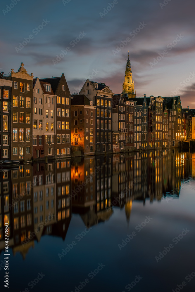 Old historical canal houses along the Damrak canal in Amsterdam at dusk
