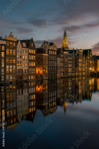 Old historical canal houses along the Damrak canal in Amsterdam at dusk