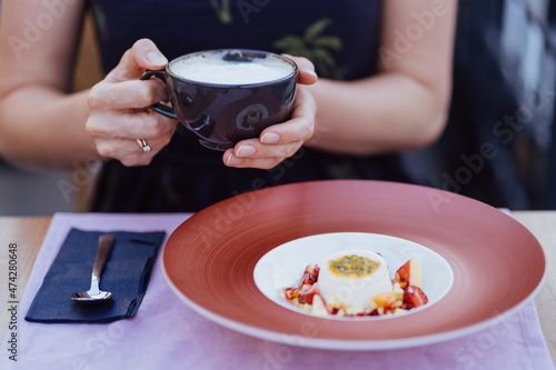 Woman holding a cup of coffee and enjoying the view of a delicious desert with fresh exotic fruits