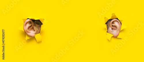 Fotografia Two woman's ear through a torn holes in yellow paper