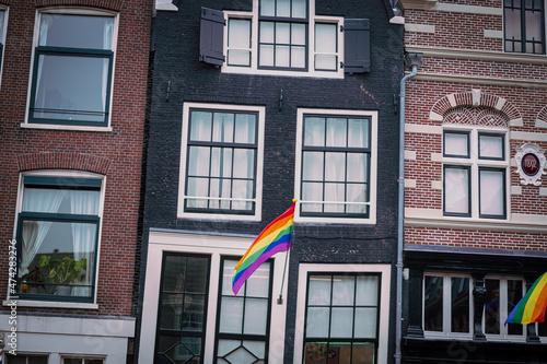 Gay flag in Amsterdam. Gay rainbow flag on a building. Rainbow flag of the LGBT community on the building on street Amsterdam. Crooked house in Amsterdam, dancing houses with gay flags