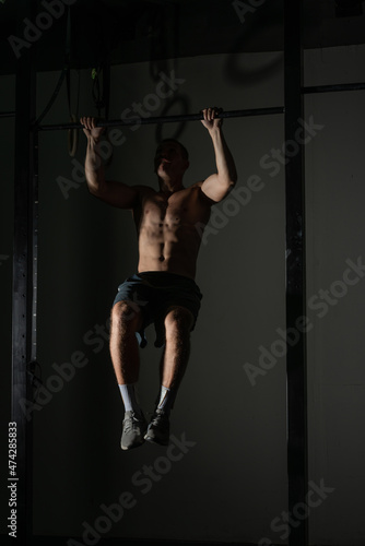 Handsome bodybuilder doing pull-ups on horizontal bar in a indoors modern gym. © qunica.com
