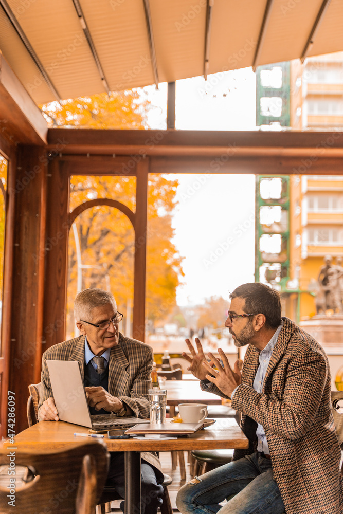 Looking at something on the lap top while discussing it in the cafe and drinking coffee Looking at something on the lap top while discussing it in the cafe and drinking coffee
