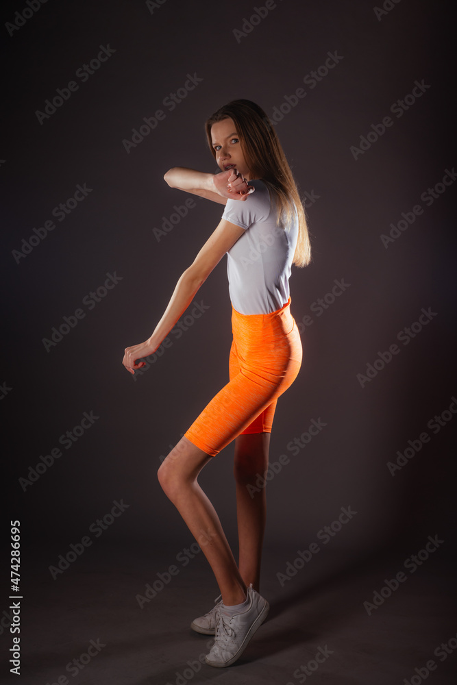Pretty sports girl with short orange leggings posing isolated on dark background in studio Pretty sports girl with short orange leggings posing isolated on dark background in studio