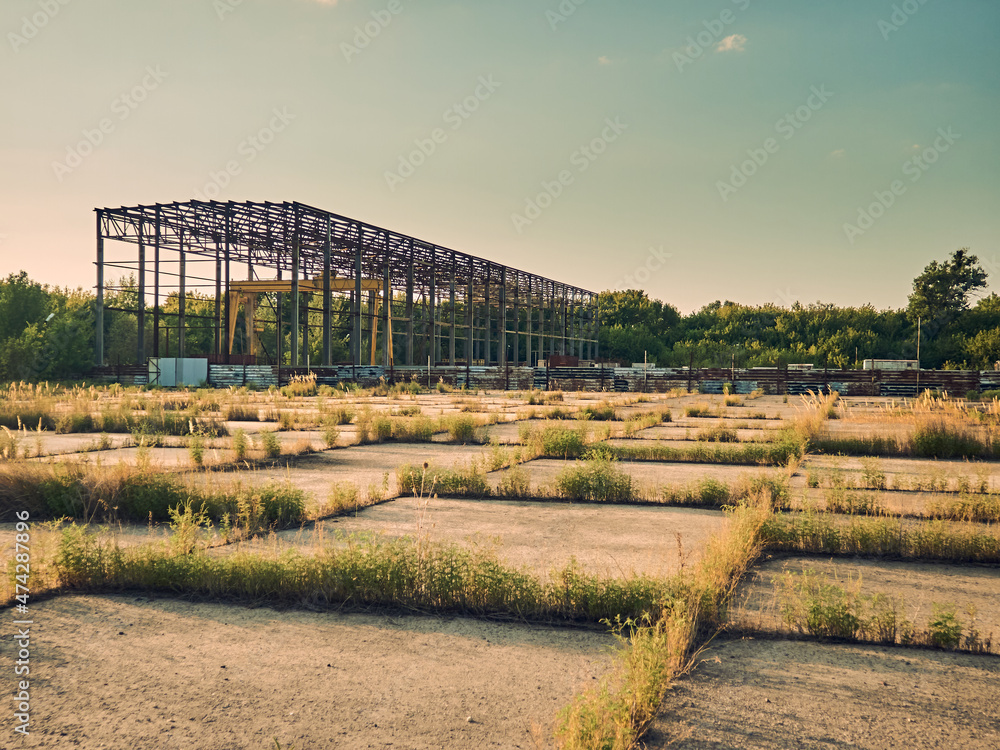 An unfinished and abandoned industrial building, grass has sprouted between concrete slabs, desolation and failure are all around