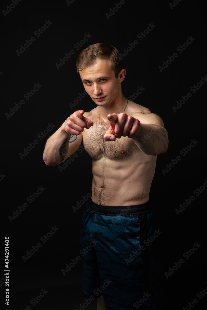Man on black background keeps dumbbells pumped up in fitness bodybuilding sexy sport, athlete weight workout lifting person weightlifting. Young sportive gym fit fingers point at us
