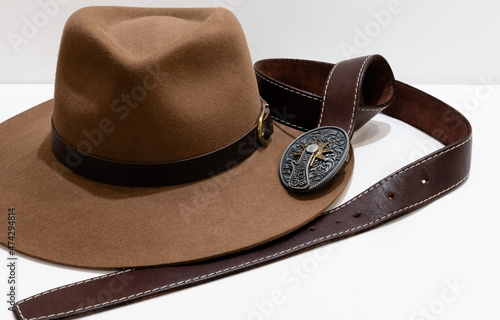 Classic cowboy brown felt hat and leather belt with vintage metal buckle on white background