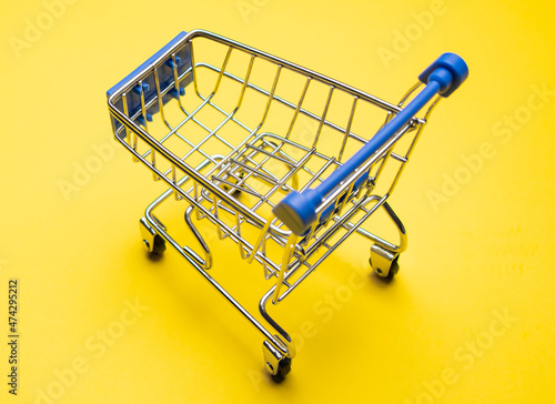 Shopping cart on yellow background. Minimalism style. Creative design. Copy space. Shop trolley at supermarket. Sale, discount, shopaholism concept. Consumer society trend.