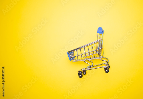 Shopping cart on yellow background. Minimalism style. Creative design. Copy space. Shop trolley at supermarket. Sale, discount, shopaholism concept. Consumer society trend.