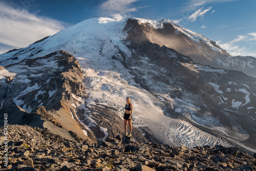 Fit female standing on a cliff next to Mount Rainier smiling at camera photo