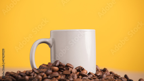 light gray mug, on a mountain of coffee beans, with yellow background