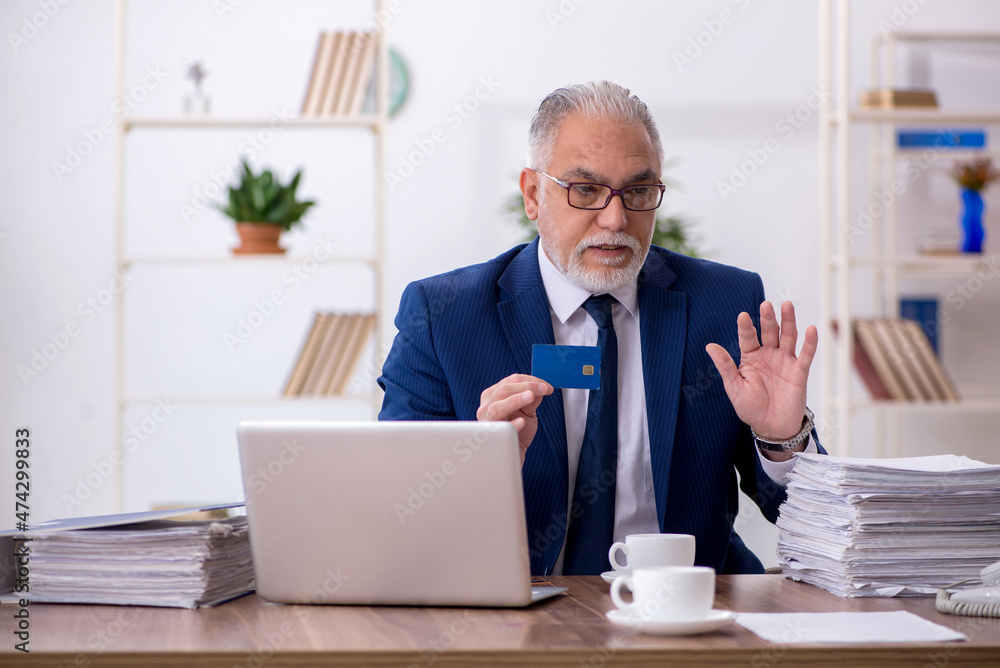 Old male employee holding credit card in the office Old male employee holding credit card in the office