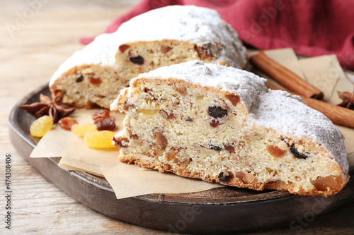 Wooden plate of cut delicious Stollen sprinkled with powdered sugar on table, closeup