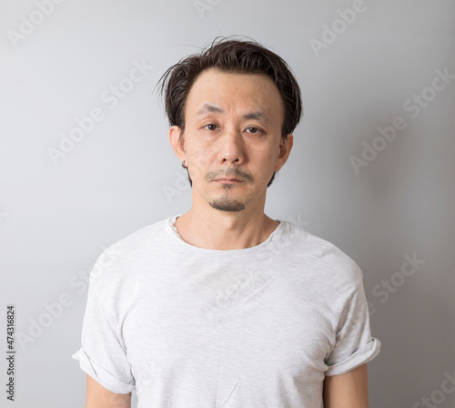 Portrait of self-confident middle age Asian man in a white t-shirt on grey background.