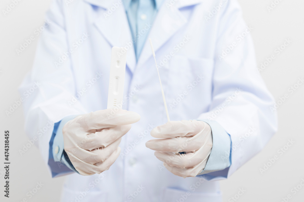 Medical personnel holding Antigen Test Kit (ATK) standing on white background.