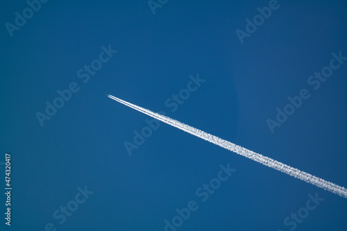 Jet airpllane with thick trace flies to the sun in deep blue sky