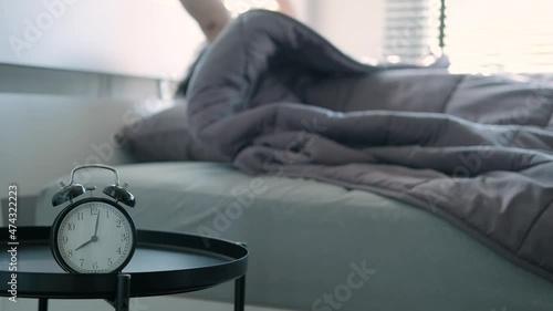 Alarm clock at 8 am in the morning man sleeping wake up press stop alarm and then continued to sleep by covaering his head with a blanket on holiday sunlight shines through the window into the bedroom