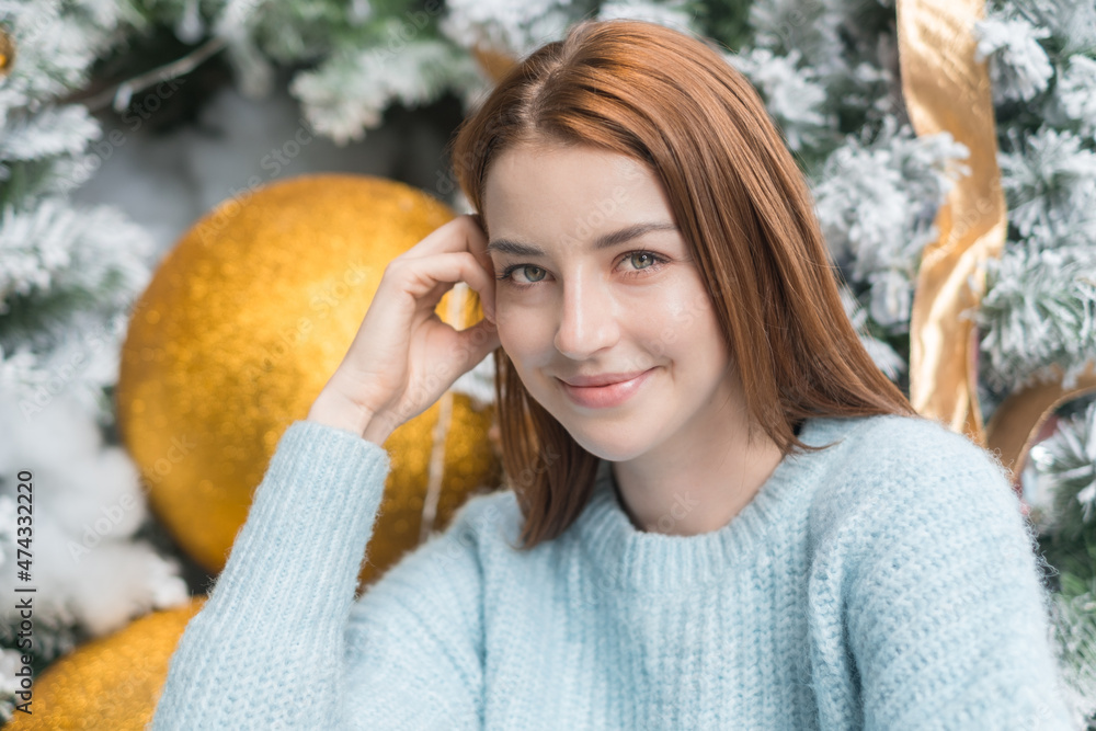 New Year close up portrait of beautiful smiling caucasian young woman in cozy wool warm light blue sweater. Christmas tree on the background. New Year close up portrait of beautiful smiling caucasian young woman in cozy wool warm light blue sweater. Christmas tree on the background.