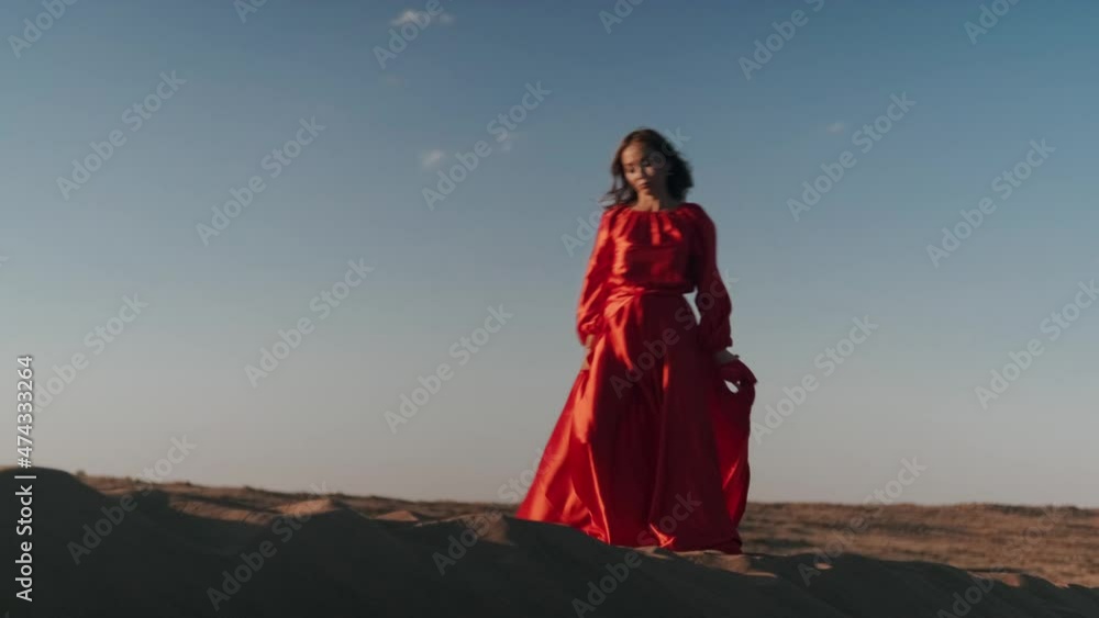 An Asian woman in a red dress gets into a pose on one leg on sand dunes An Asian woman in a red dress gets into a pose on one leg on sand dunes