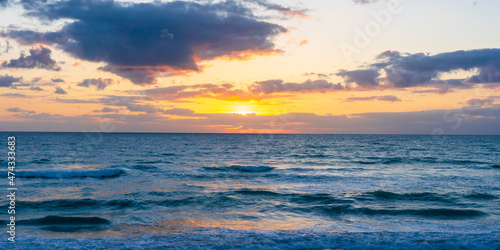 Sunrise over the Atlantic Ocean in Florida. The bright yellows of the sky contrast with the deep blue of the ocean waves. Glare of reflected light in waves