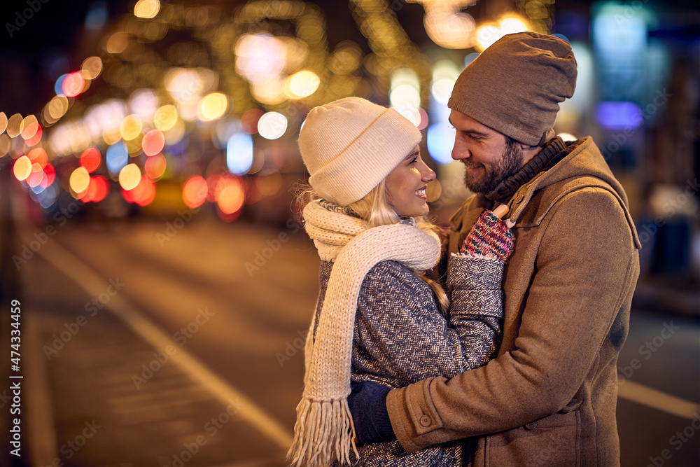 A young couple in love is in a hug while enjoying a walk the city during christmas holidays. Christmas, city, relationship