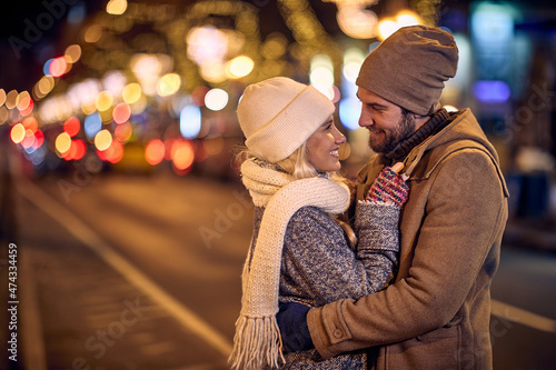 A young couple in love is in a hug while enjoying a walk the city during christmas holidays. Christmas, city, relationship