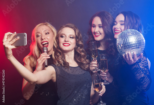 Close-up shot of group of laughing women wearing black dresses having party, take selfie with smartphone