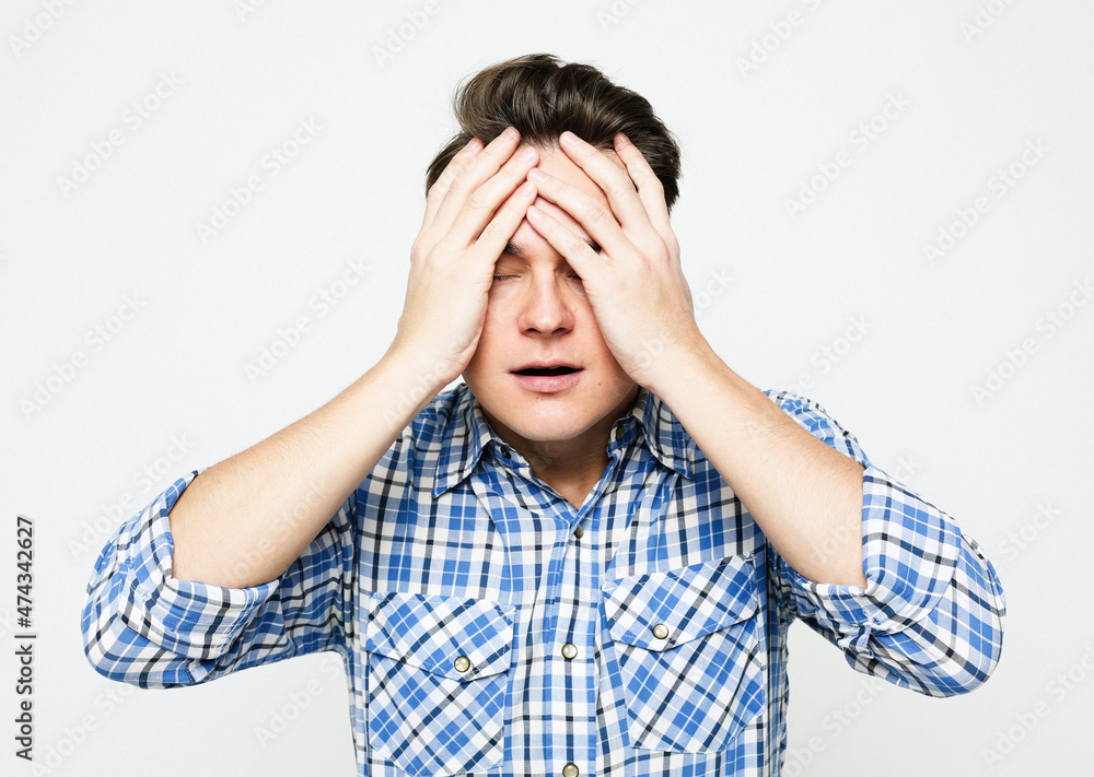 Young handsome man covering eyes with hands isolated over grey background Young handsome man covering eyes with hands isolated over grey background