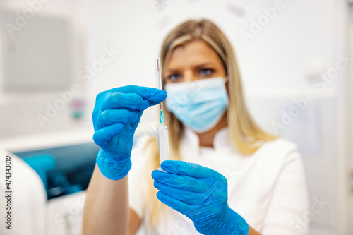 Cure, vaccine, and treatment. A nurse standing in a laboratory and holding a syringe with a needle. Selective focus on hands and the cure.