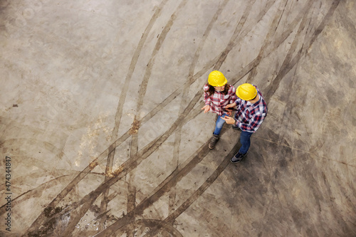 Construction supervision. Construction manager with the client. The man and a woman with protective helmet talk about the project and a walk on the concrete floor with muddy tire print photo