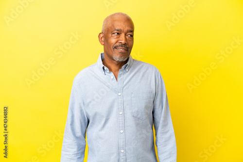 Cuban Senior isolated on yellow background having doubts while looking side