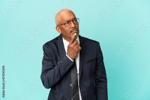 Business senior man isolated on blue background having doubts while looking up