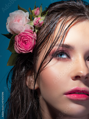 A young beautiful woman with rose flowers in her wet hair. Portrait of a beautiful brunette with perfect skin, close-up on a blue background © Ulia Koltyrina