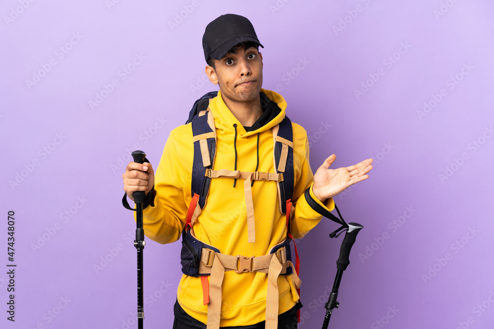 African American man with backpack and trekking poles over isolated background having doubts while raising hands African American man with backpack and trekking poles over isolated background having doubts while raising hands