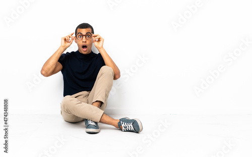 African American man sitting on the floor with glasses and surprised