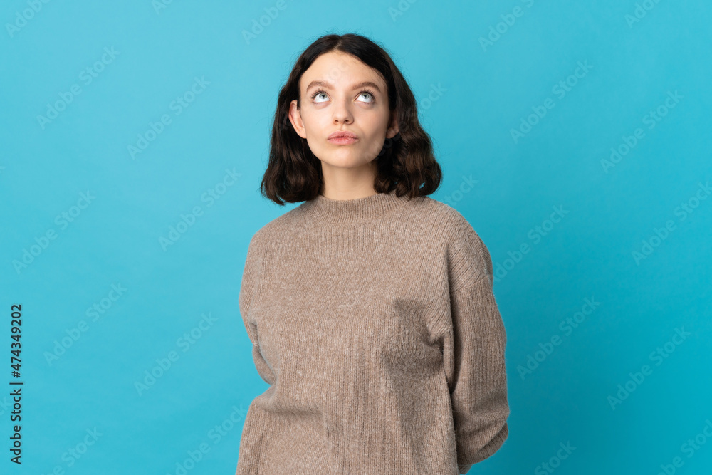 Obraz premium Teenager Ukrainian girl isolated on blue background and looking up